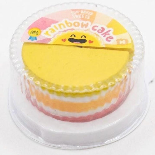 Yellow and pink layered cake in a clear plastic container with a rainbow-themed lid.