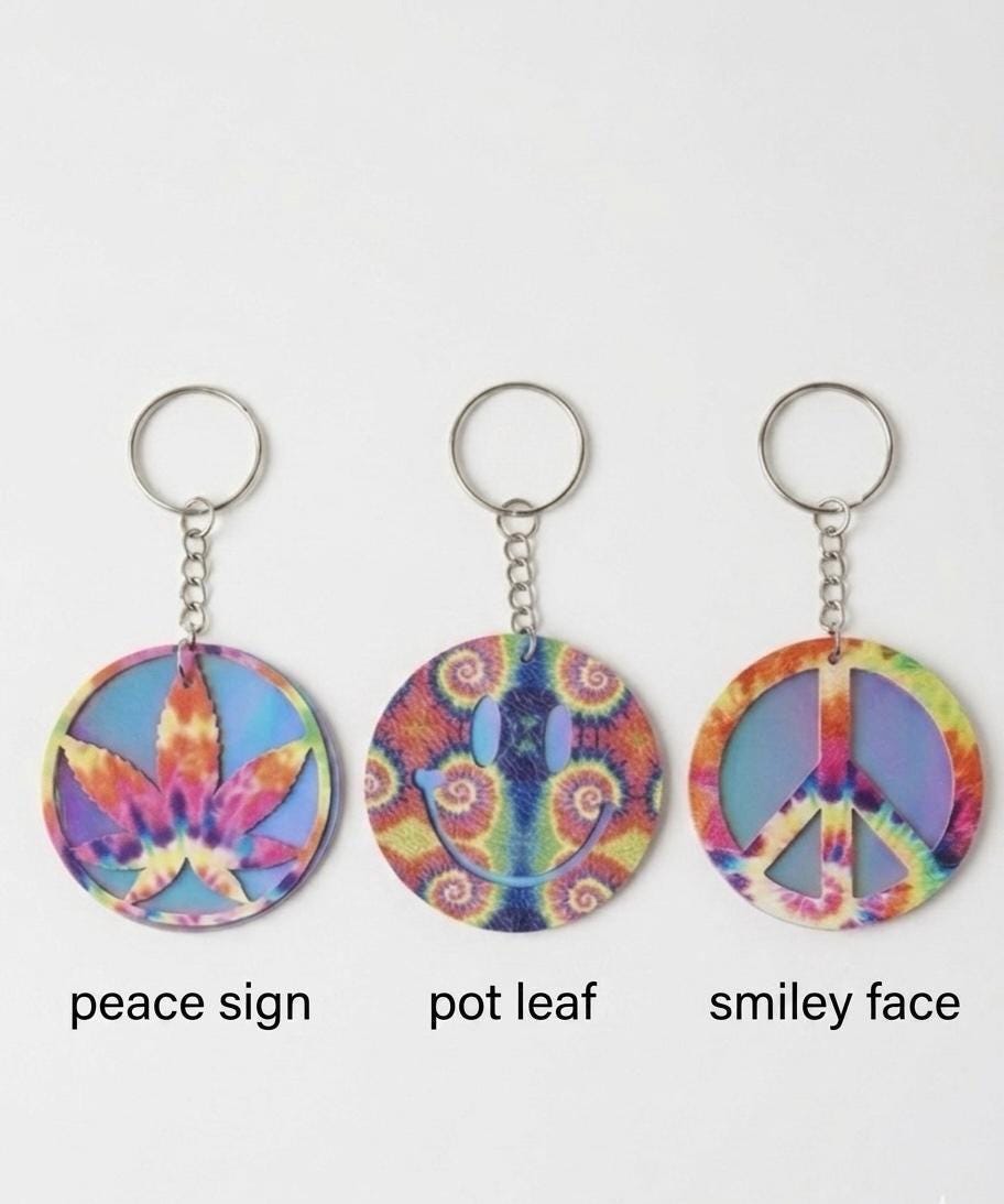 Three tie-dye keychains with peace sign, pot leaf, and smiley face designs on a white background.